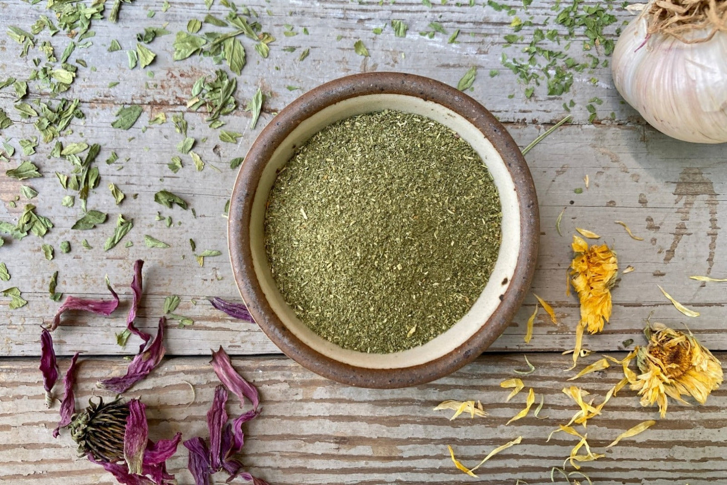 A jar of Emerald Mountain Dust from Well Seasoned Table on a wooden background with a sprinkle of calendula flowers and dried ramps.