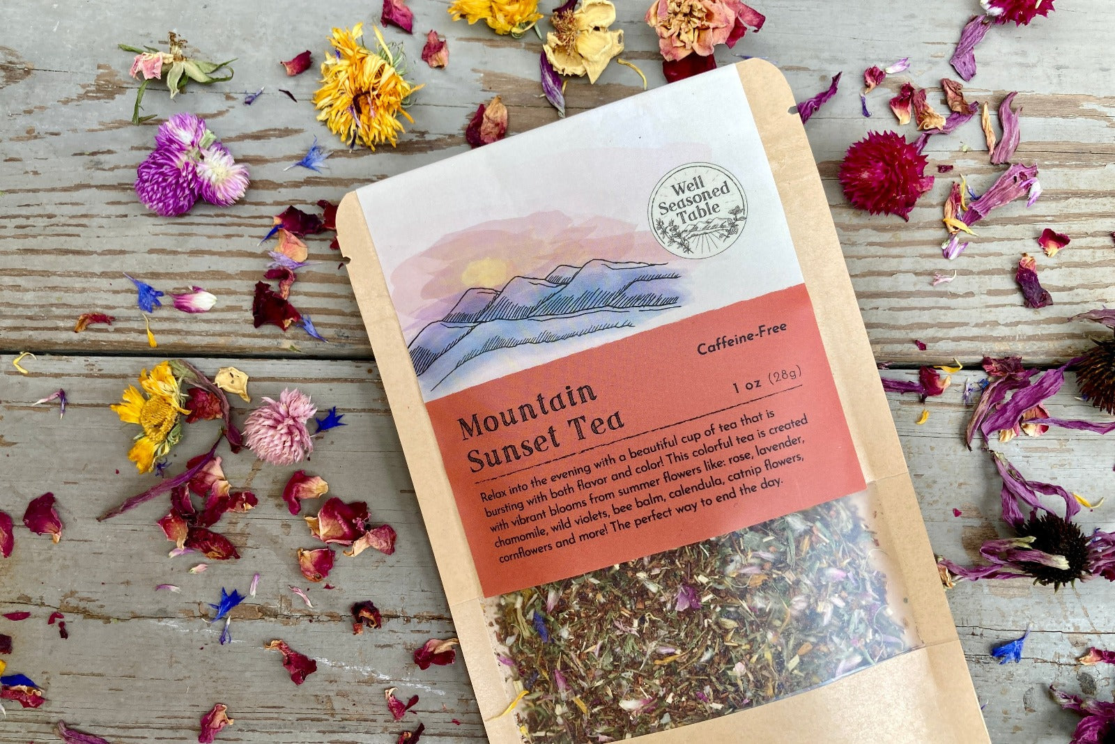 Up close of a packet of Mountain Sunset Tea on a wooden background surrounded by colorful dried flowers.