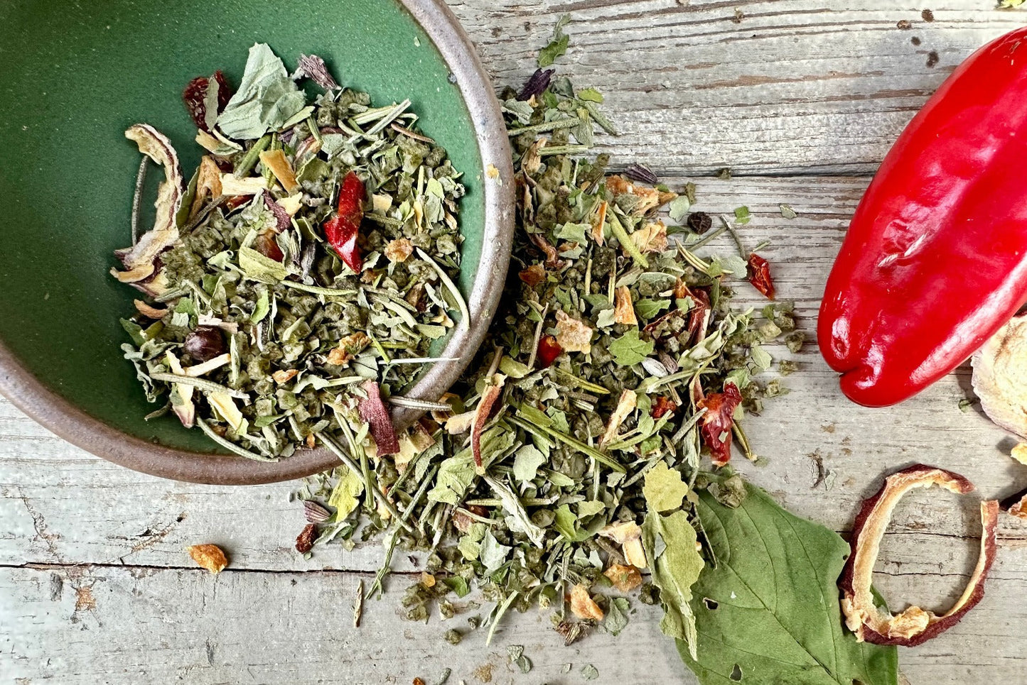 A bowl of Rosemary Basil Sea Salt from Well Seasoned Table with peppers, rosemary, and basil around it.